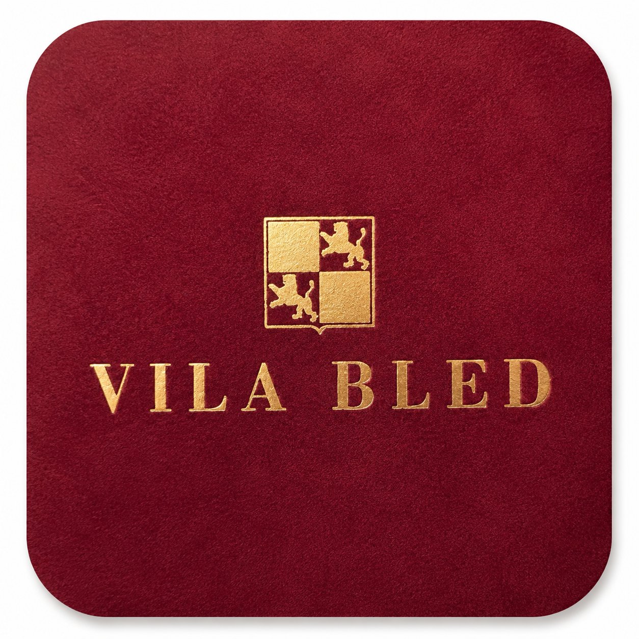 Detajl zlatotiska logotipa in napisa 'VILA BLED' na bordo rdeči žametni podlagi z zaobljenimi robovi.
